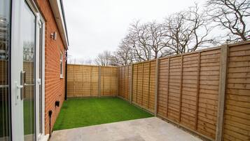 A backyard with a green lawn, a wooden fence, and a brick wall.