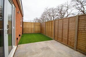 A backyard with a green lawn, a wooden fence, and a brick wall.