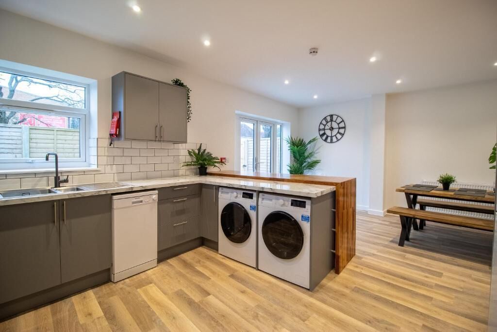 A modern kitchen with built-in appliances, a wooden dining table, and a bench.