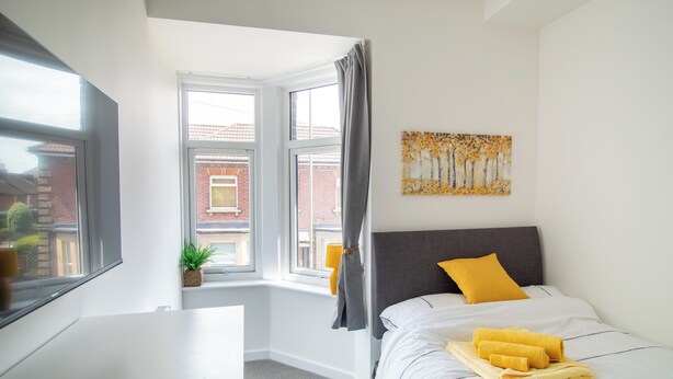 A hotel room with a bed, a desk, a window with a view of buildings, and a painting on the wall. - 29 Twyford (Eastleigh)