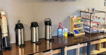 Una estación de café con tres tazas térmicas de acero inoxidable, una cafetera y una variedad de granos de café y azúcar.