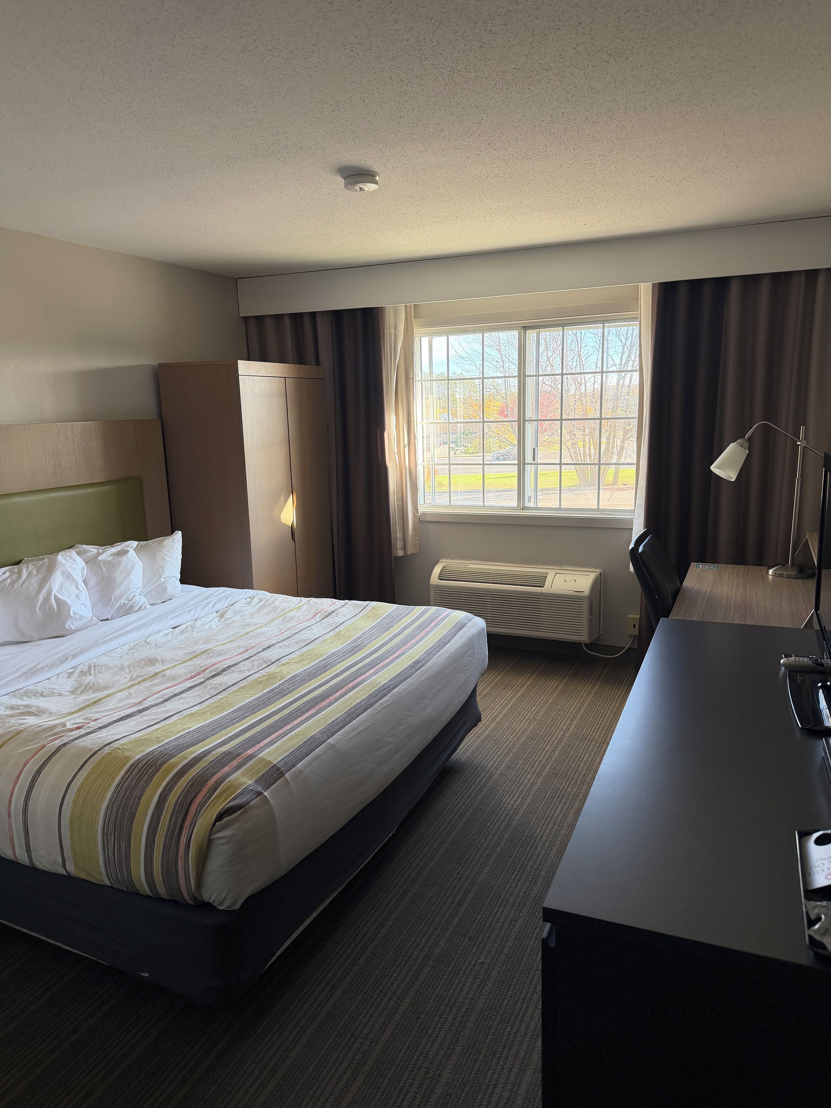 A hotel room with a bed, a desk, a window with curtains, and a ceiling light.