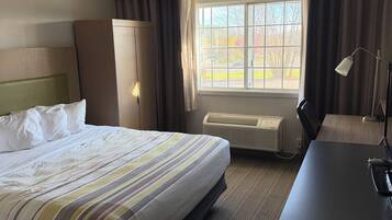 A hotel room with a bed, a desk, a window with curtains, and a ceiling light.