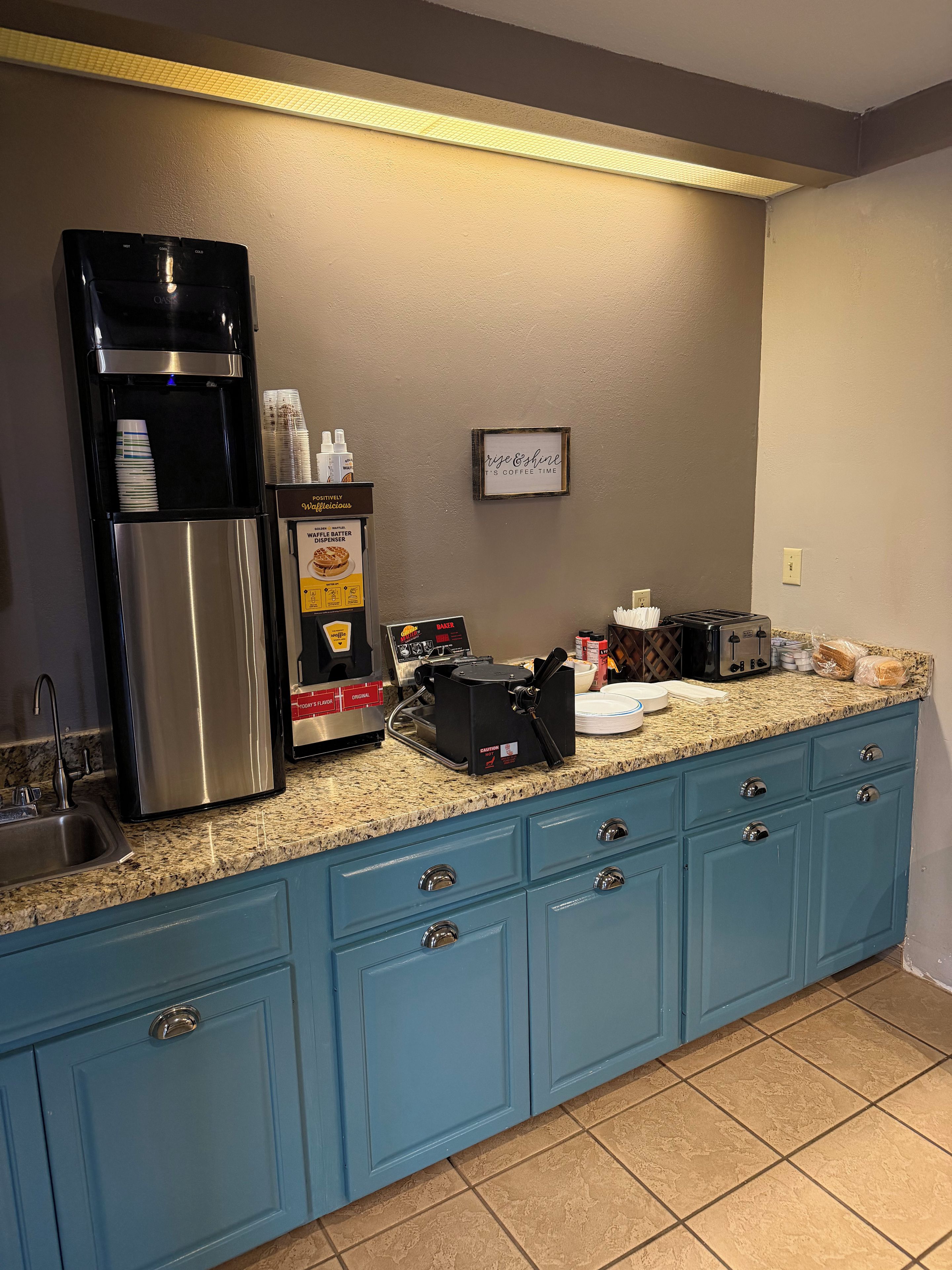Una cocina con una cafetera, un dispensador de masa para gofres y un tostador sobre la encimera.