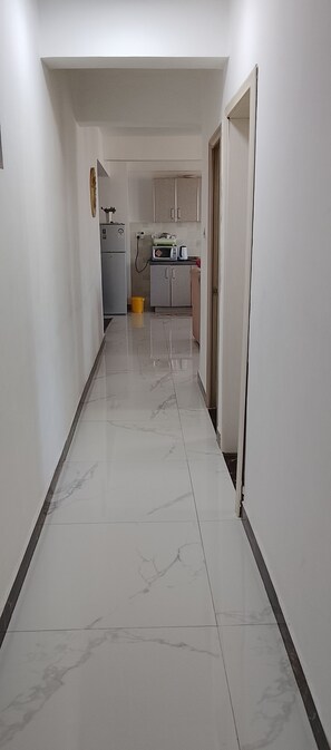 A corridor with a kitchen area at the end, featuring cabinets, a microwave, and a refrigerator. - Cozy 2-bedroom apartment in the heart of Kilimani near Yaya Center in Nairobi (Nairobi)