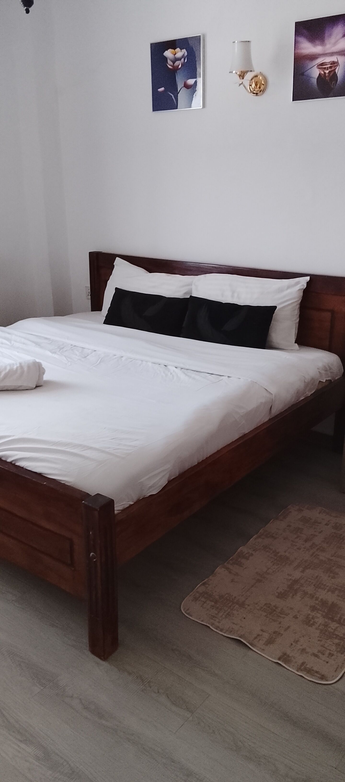 Un lit avec une literie blanche, une tête de lit marron et un tapis marron sur un plancher en bois.