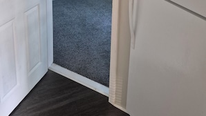 A room with a white door, a white refrigerator, and a grey carpet.