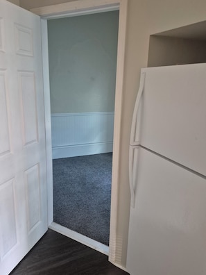 A room with a white door, a white refrigerator, and a grey carpet.