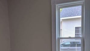 A room with a large window, white wainscoting, and a dark carpet.