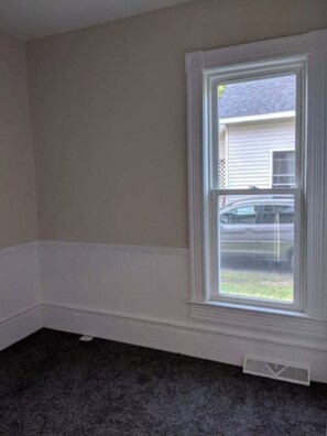 A room with a large window, white wainscoting, and a dark carpet.
