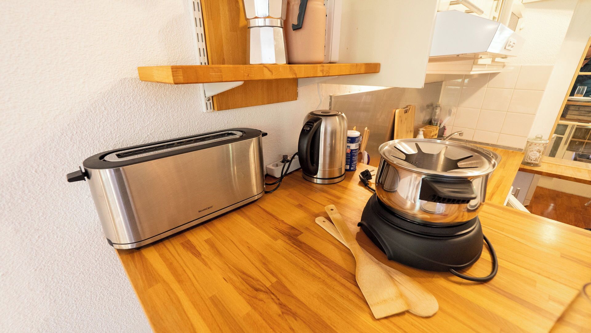 A kitchen with a toaster, a kettle, a pot, and wooden utensils on the counter.