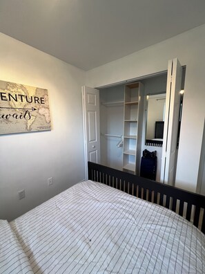 A bedroom with a bed, a wardrobe, a mirror, and a wall-mounted artwork.