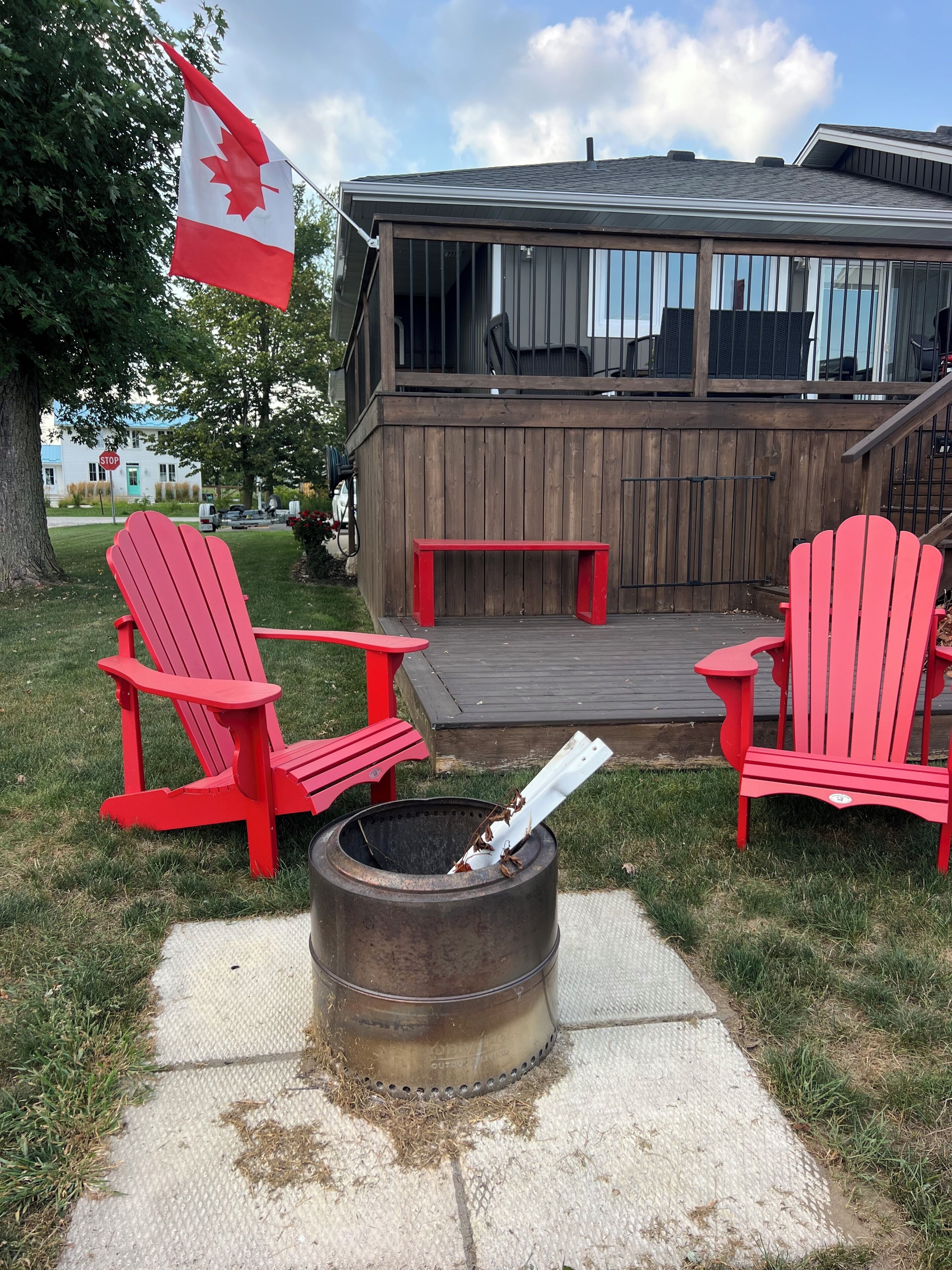 Eine Terrasse mit roten Adirondack-Stühlen, einem Feuerkorb und einer kanadischen Flagge.
