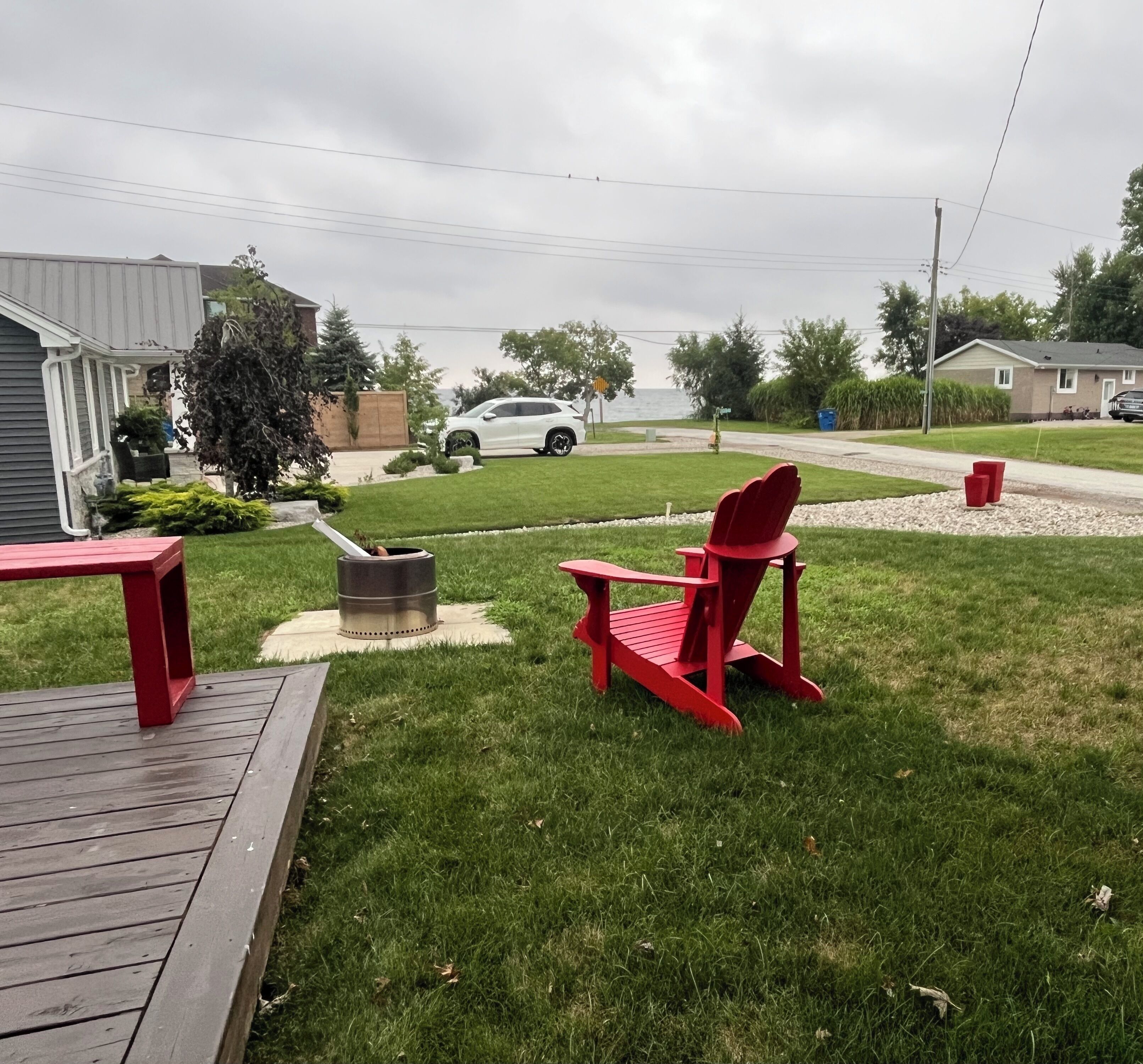 A backyard with a grill, a red chair, and a wooden deck.