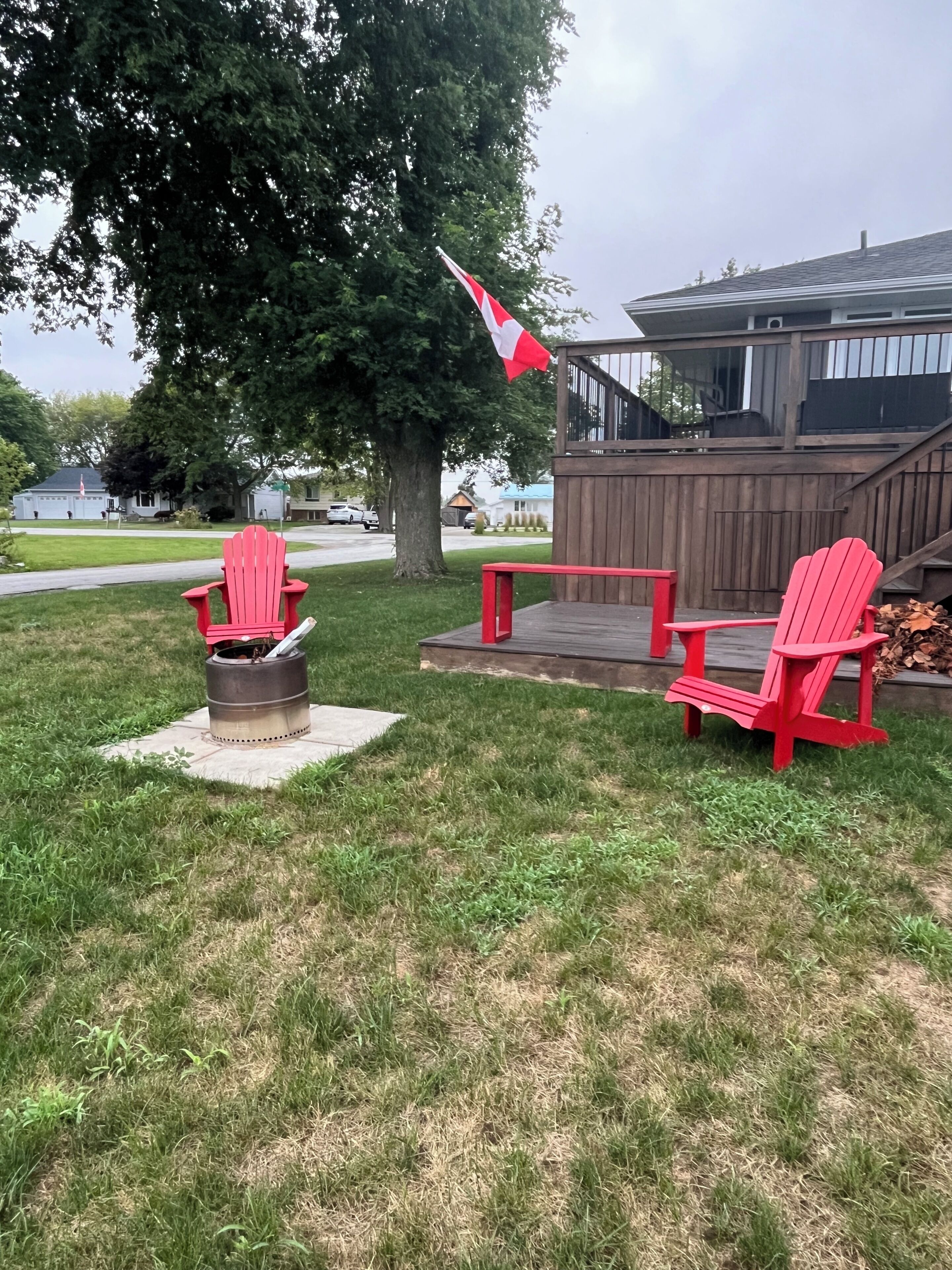 A backyard with a fire pit, two Adirondack chairs, and a wooden deck.