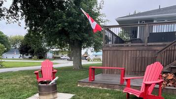 A backyard with a fire pit, two Adirondack chairs, and a wooden deck.