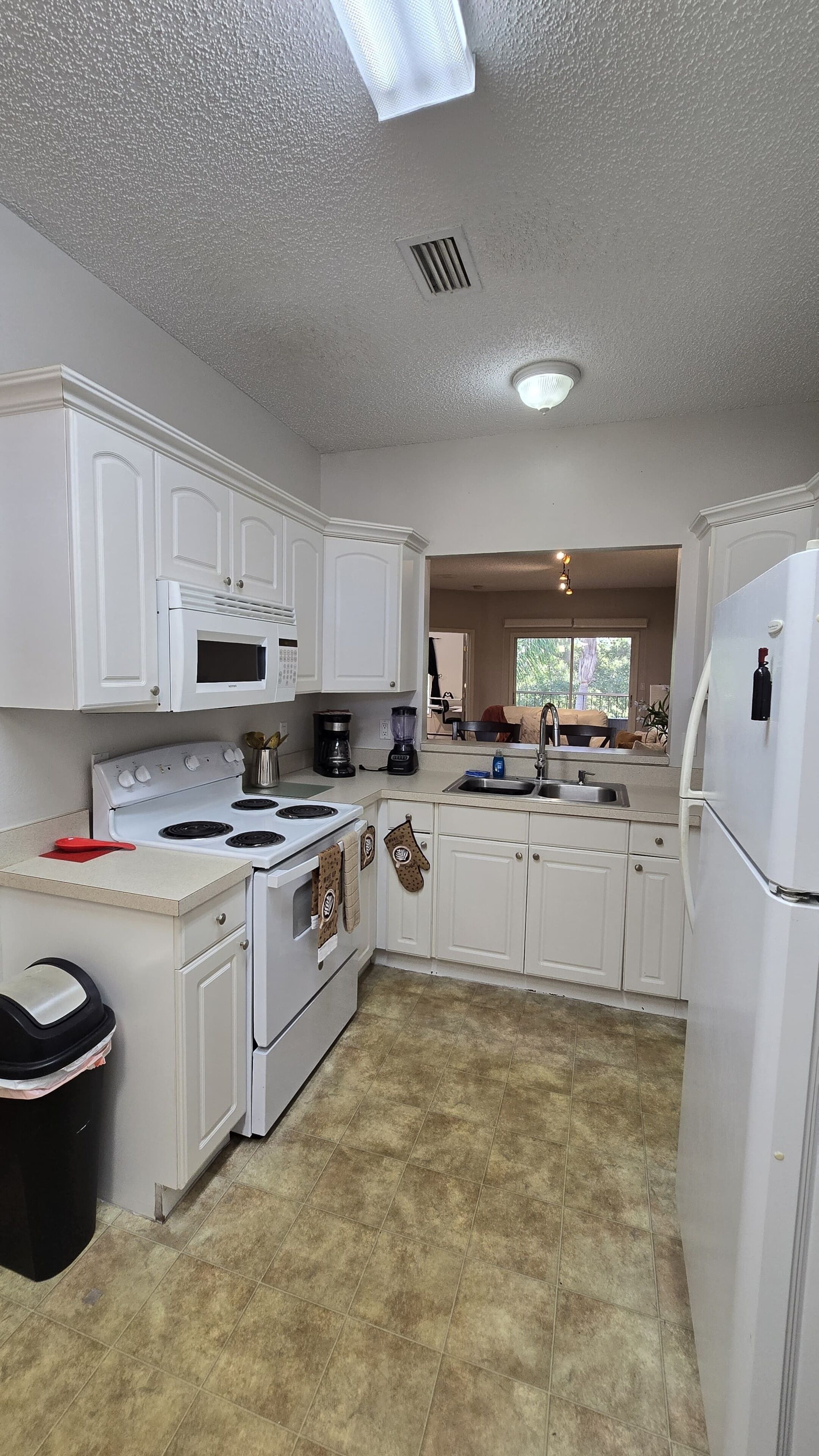 A kitchen with white cabinets, a stove, a microwave, and a refrigerator.