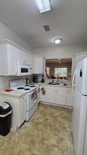 A kitchen with white cabinets, a stove, a microwave, and a refrigerator. - Cozy 2-bedroom apartment 15 minutes away from Disney Parks. FREE PARKING (Kissimmee)