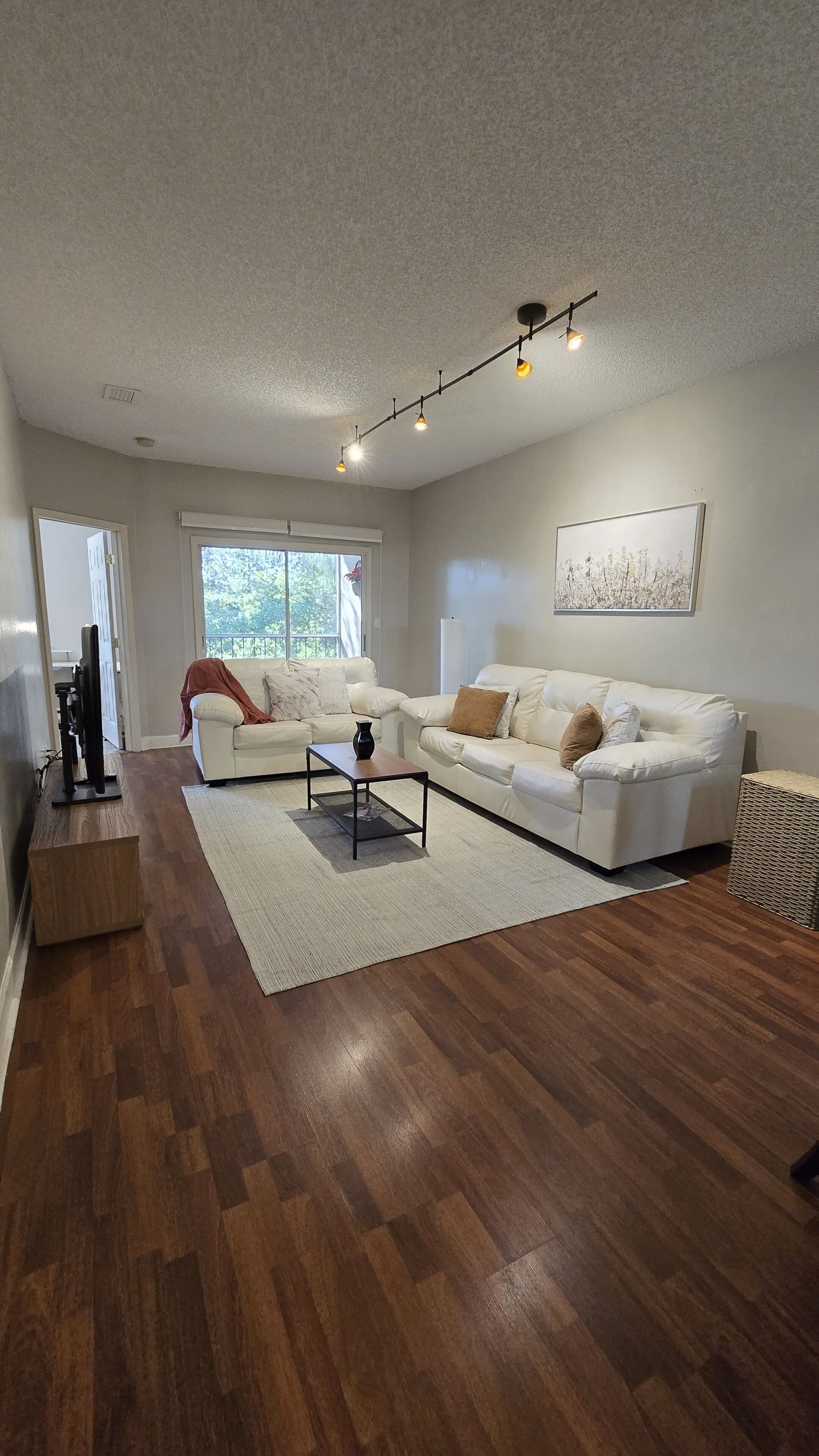 A modern living room with a white sofa, a coffee table, and a flat-screen TV.