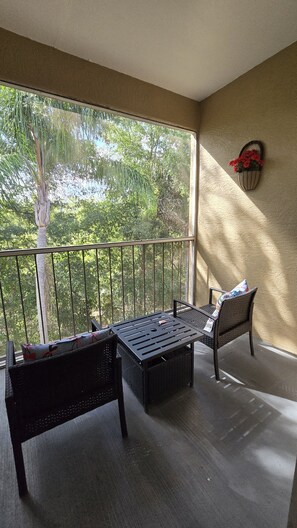 A balcony with a table and two chairs, a potted plant, and a wall-mounted basket. - Cozy 2-bedroom apartment 15 minutes away from Disney Parks. FREE PARKING (Kissimmee)