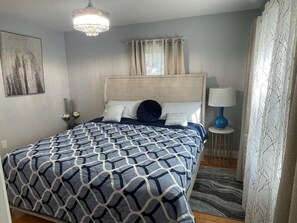 A bedroom with a bed, a chandelier, a bedside lamp, and a window with curtains. - Amazing Boston Downtown City View Rooms (BOSTON)