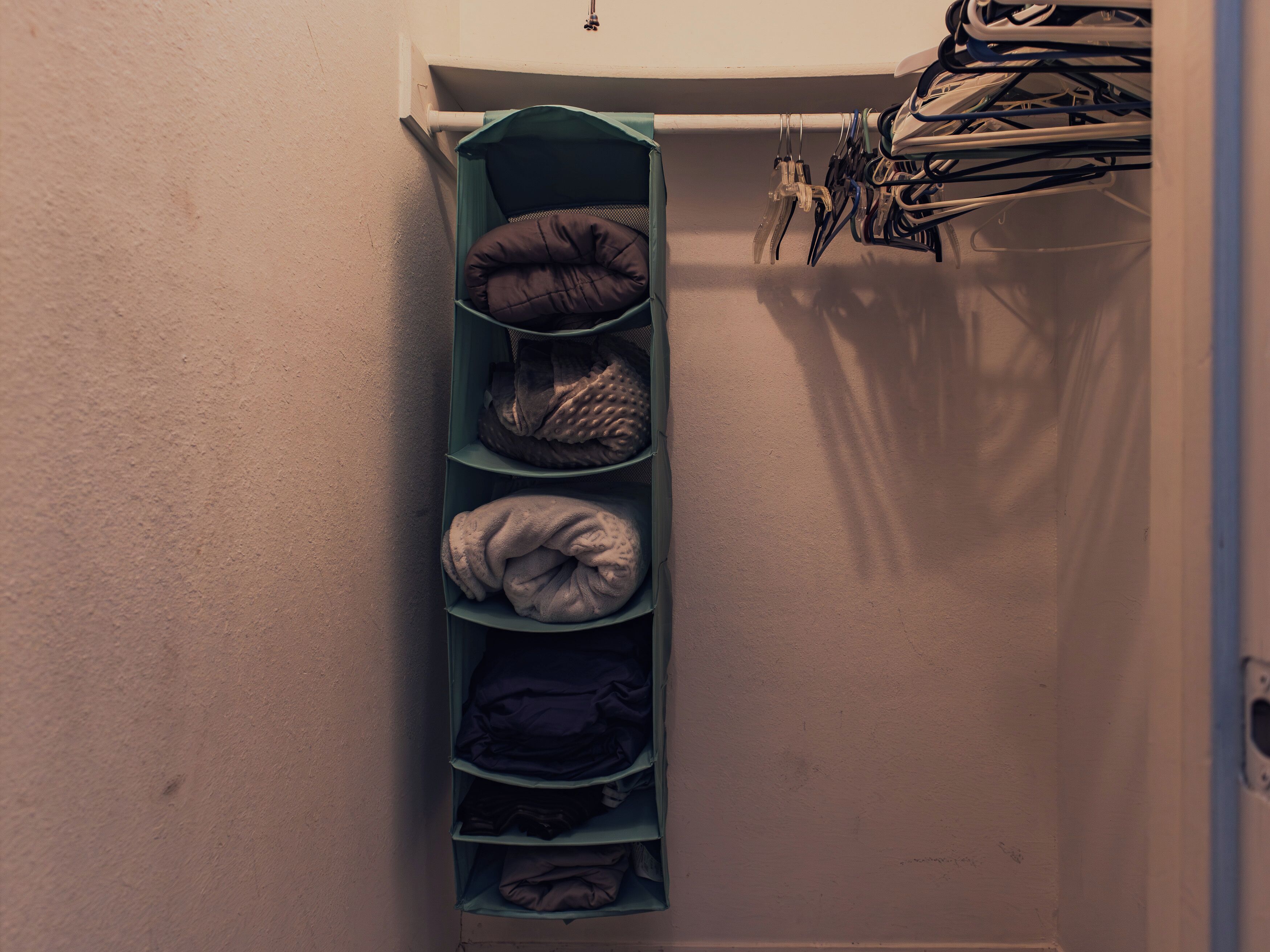 Un placard avec des étagères où sont pliés des vêtements et une tringle où sont suspendues des chaussures.
