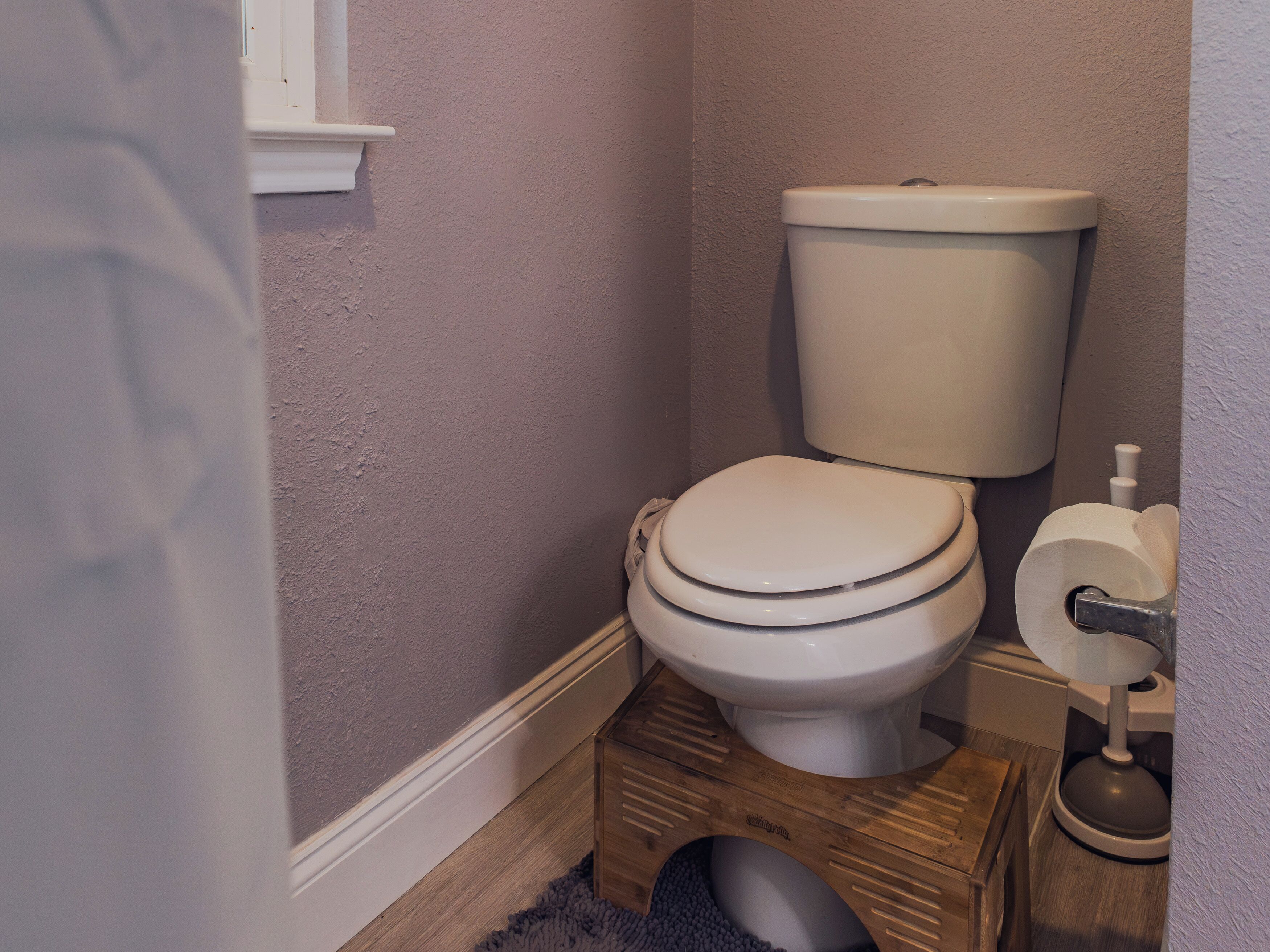 Un baño pequeño con un inodoro, un taburete de madera y un rollo de papel higiénico.
