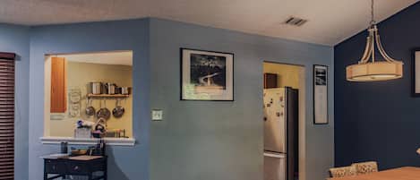 A modern kitchen with a built-in oven, a dining area with a wooden table and patterned chairs, and a ceiling light fixture.