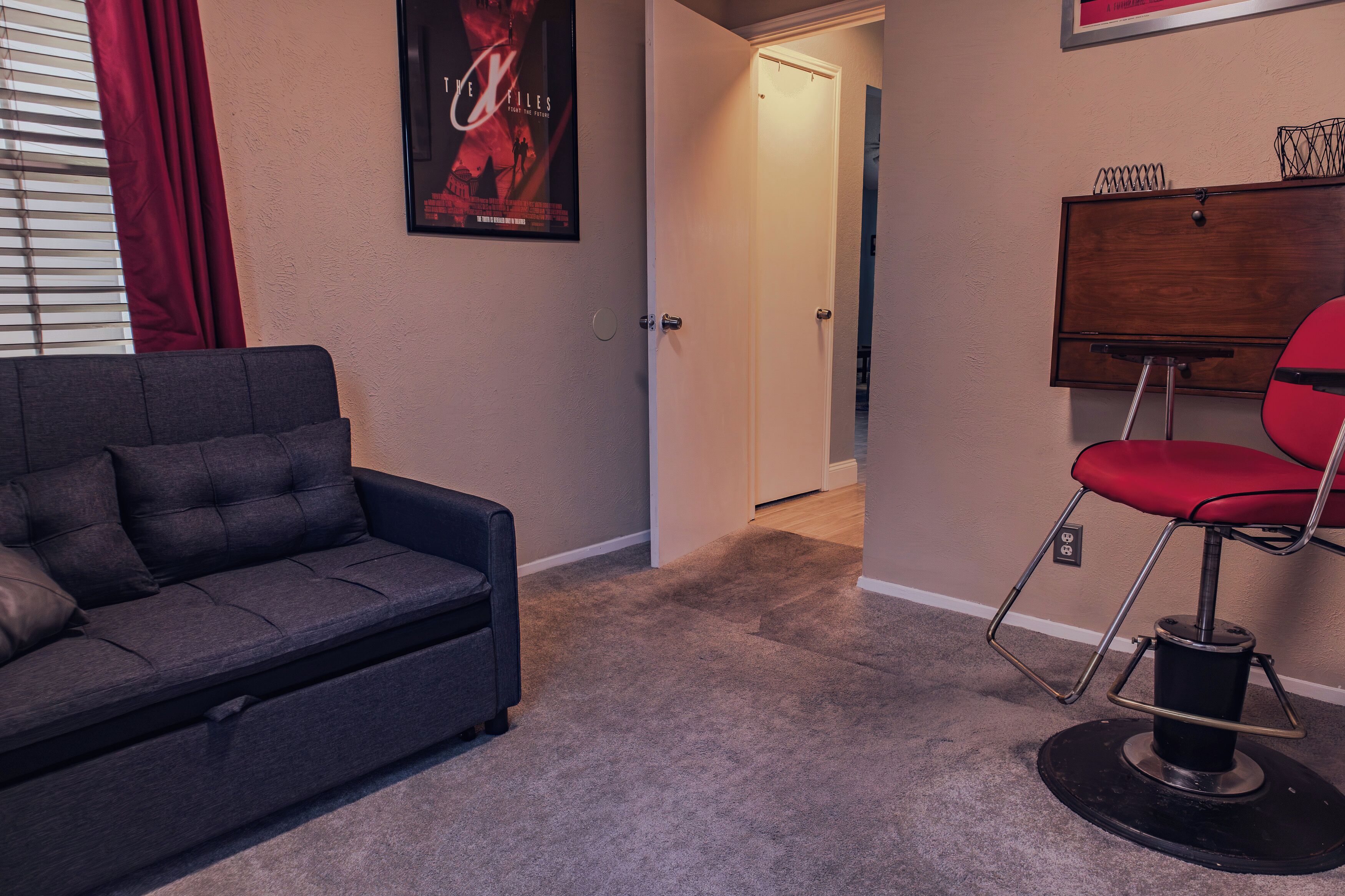 A room with a grey sofa, a red chair, a poster on the wall, and a door leading to another room.