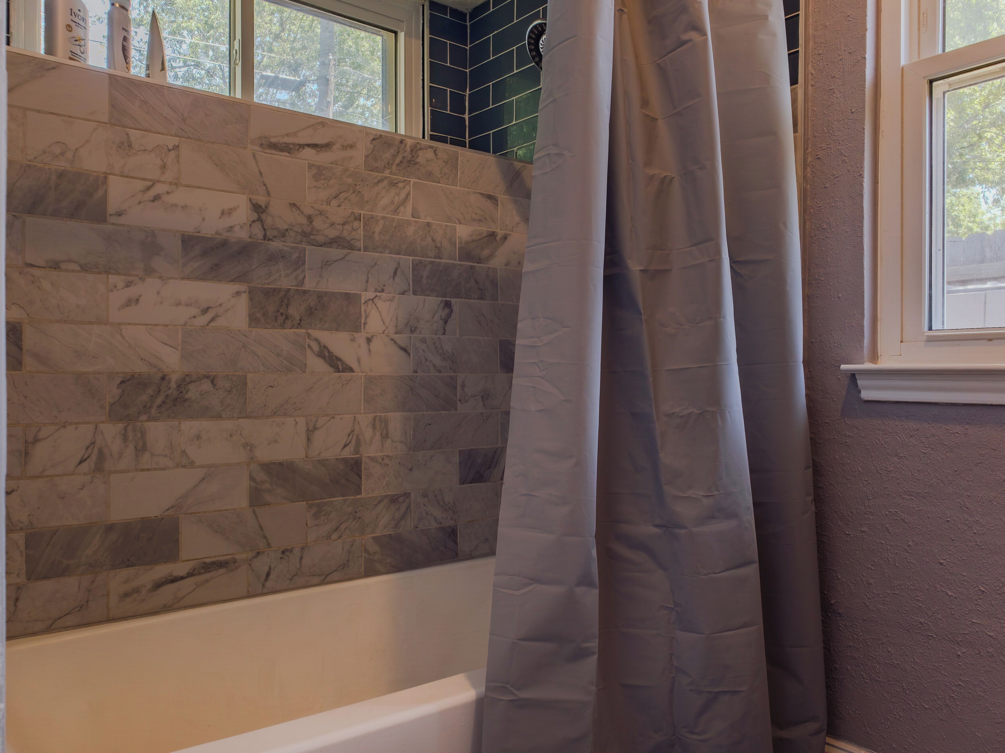 A bathroom with a marble tile wall, a bathtub, and a window with a view of trees.