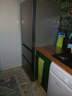 A compact kitchen with a stainless steel refrigerator, a white dishwasher, and a wooden countertop. - Devorgilla View – Bright & Spacious 2-Bed Apartment (Dumfries and Galloway)