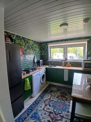 A compact kitchen with a washing machine, a refrigerator, a microwave, and a window with a view of the outside. - Devorgilla View – Bright & Spacious 2-Bed Apartment (Dumfries and Galloway)