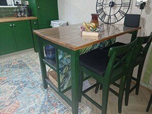 A kitchen with a wooden table, green chairs, a clock, and a patterned rug. - Devorgilla View – Bright & Spacious 2-Bed Apartment (Dumfries and Galloway)