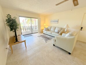 A living room with a sofa, a coffee table, a lamp, a plant, and a view through a sliding glass door.