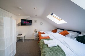 Une chambre avec deux lits, une télévision, un bureau et une fenêtre de toit.