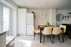 Une cuisine moderne avec un coin repas, des meubles blancs et une grande fenêtre. Une horloge est accrochée au mur.