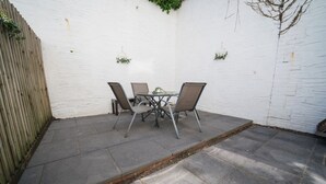Ein Patio mit Tisch und Stühlen, einer weißen Wand und einem Holenzaun.