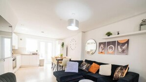 Ein modernes Wohnzimmer mit einer schwarzen Couch, einem Essbereich und einer Küche im Hintergrund.