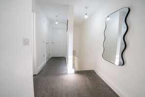 A hallway with a carpeted floor, white walls, and a large, wavy mirror on the right. - Premium 3 Bed Cardiff City Sleeps 9 with Free Parking (Cardiff)