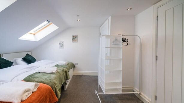 Ein Schlafzimmer mit einem Oberlicht, einem Bett mit grüner Decke, einem weißen Kleiderschrank und einer weißen Regalwand.