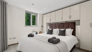 Ein modernes Schlafzimmer mit einem großen Bett, einem Fenster mit Blick auf Grünflächen und integrierten Schränken.