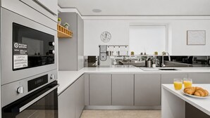 Eine moderne Küche mit integrierten Geräten, einer zentralen Kochinsel und einer Frühstücksecke mit Croissants und Orangensaft.