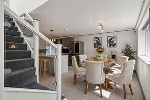 Cozinha moderna com área de refeições, apresentando uma escada com guarda-corpo de vidro, uma mesa de jantar posta para quatro e uma ilha de cozinha.