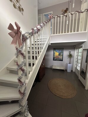 A staircase with a decorative garland and bow, leading to a second-floor landing with a bench and a potted plant. - House with a completely private pool and hot tub near Paris (bures sur yvette)