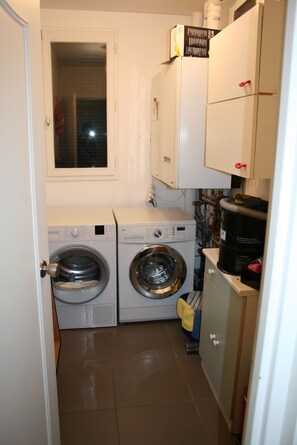 A compact laundry room with two front-loading washing machines, a window, and a small cabinet with a red handle. - House with a completely private pool and hot tub near Paris (bures sur yvette)