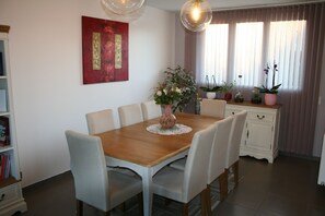 Ein Essbereich mit Holztisch, weiß gepolsterten Stühlen, einer Blumenvase und einem Bild an der Wand.
