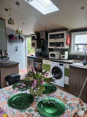 A compact kitchen with a washing machine, microwave, and a small dining area with green plates. - Peacock Lodge Quirky & Tranquil Home Away from Home (Perth and Kinross)