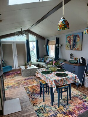 A cozy living room with a dining area, a peacock window, and a colorful elephant painting. - Peacock Lodge Quirky & Tranquil Home Away from Home (Perth and Kinross)