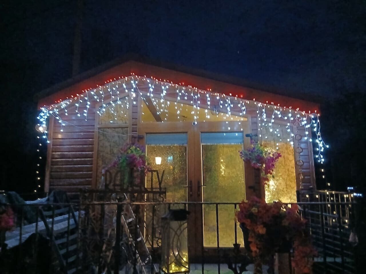 Una cabaña de madera con un porche cubierto, decorada con luces colgantes y plantas en macetas.