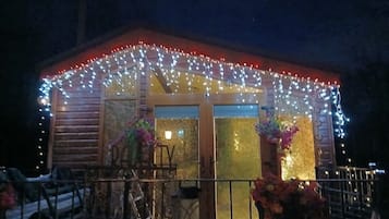 A wooden cabin with a covered porch, adorned with string lights and potted plants.
